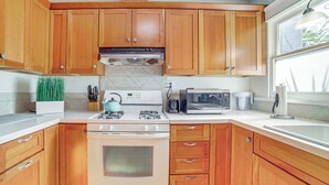 Une cuisine dotée de meubles en bois, d’une cuisinière, d’un four à micro-ondes et d’une fenêtre laissant entrer la lumière naturelle.
