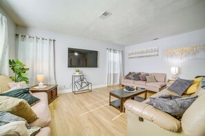 A living room with a beige sofa, a coffee table, a TV mounted on the wall, and a plant on a side table. - Family-friendly Home 2 Mi to Dtwn Riverside (Riverside)