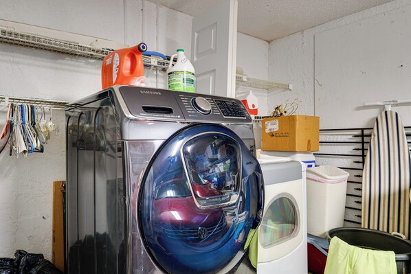 Une petite buanderie équipée d’un lave-linge à chargement frontal, d’un étendoir et d’une boîte en carton posée sur le dessus de la machine.