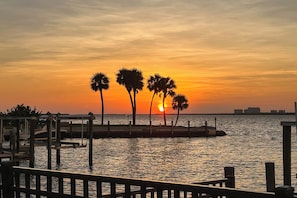 Vista del atardecer desde un paseo marítimo con palmeras y un muelle.