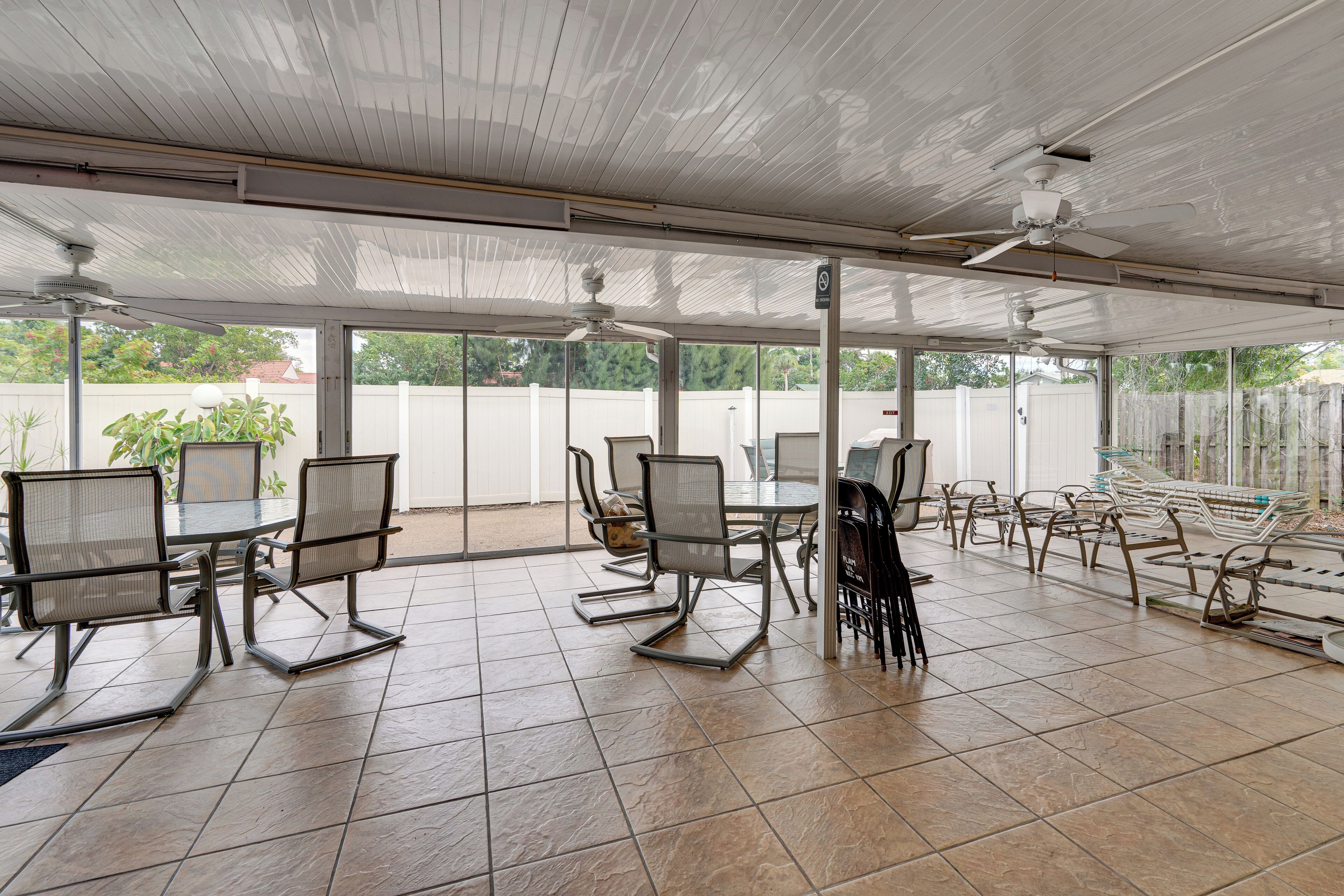 Un patio cubierto con mesas y sillas, ventanas amplias y ventiladores de techo.