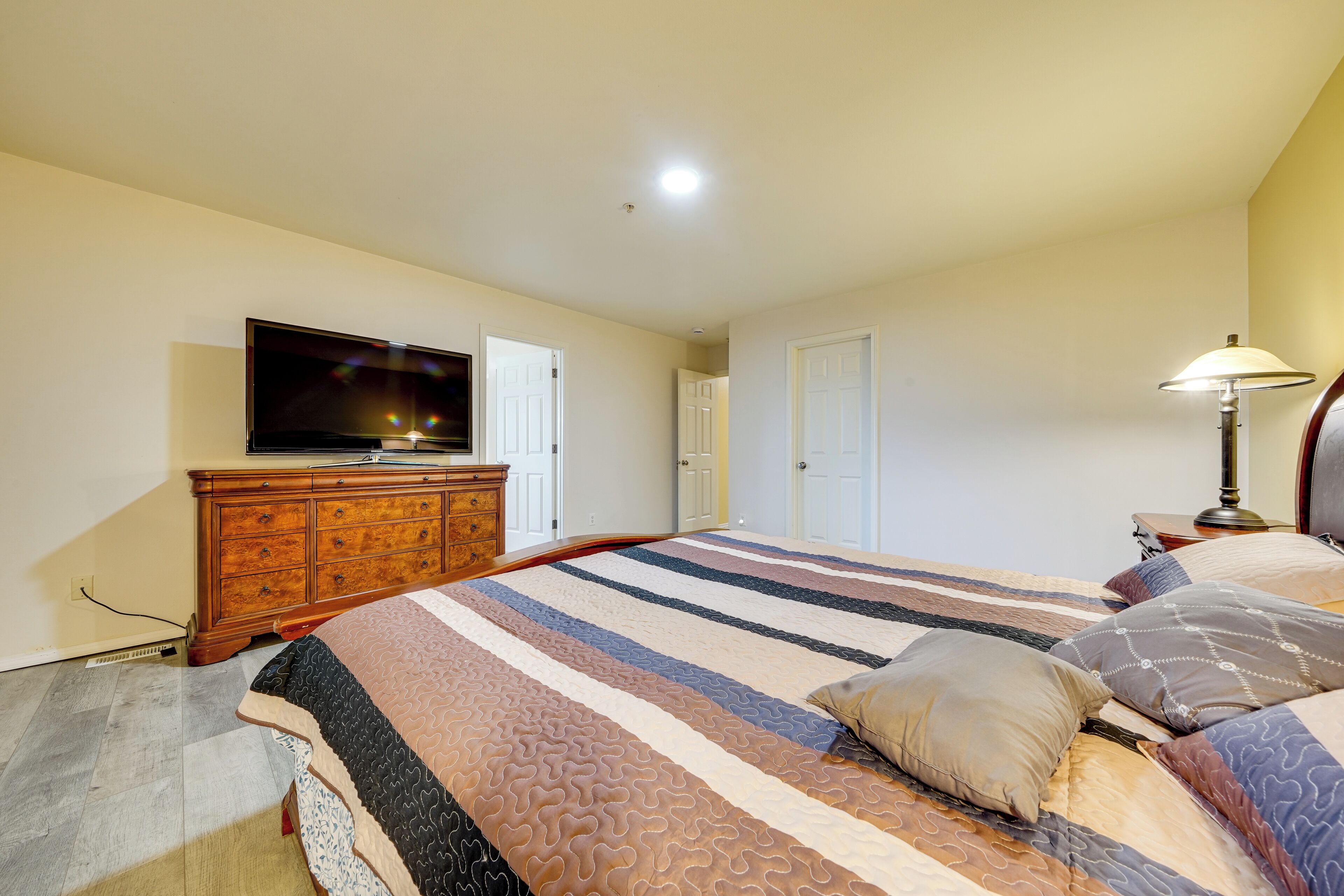 A bedroom with a large bed, a dresser, a television, and a lamp.