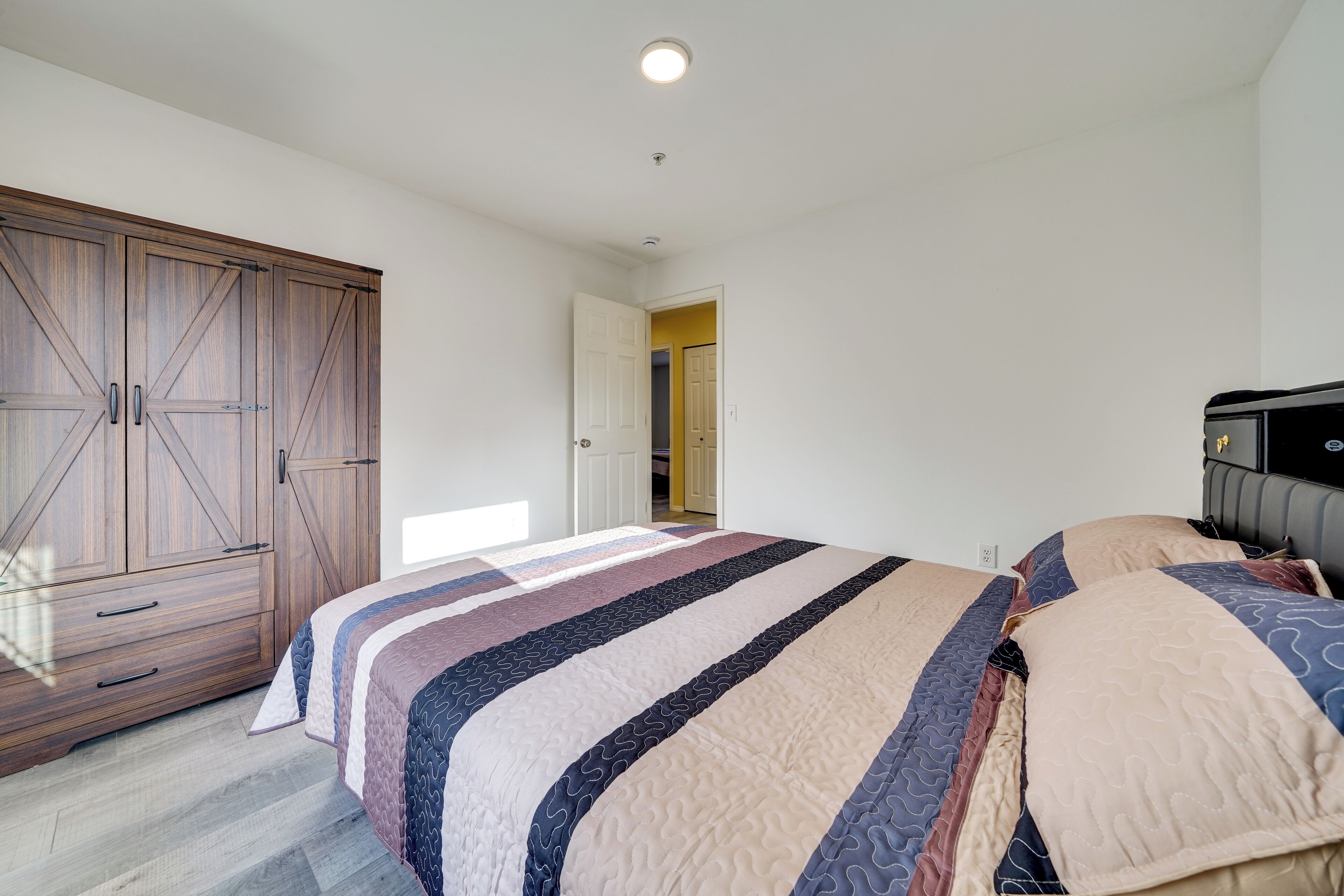 A bedroom with a large wardrobe, a bed with patterned bedding, and a door leading to another room.