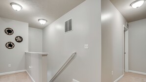 Ein Flur mit Teppichboden, einer weißen Wand mit Lüftungsgitter und drei an der Wand befestigten Wandplatten.
