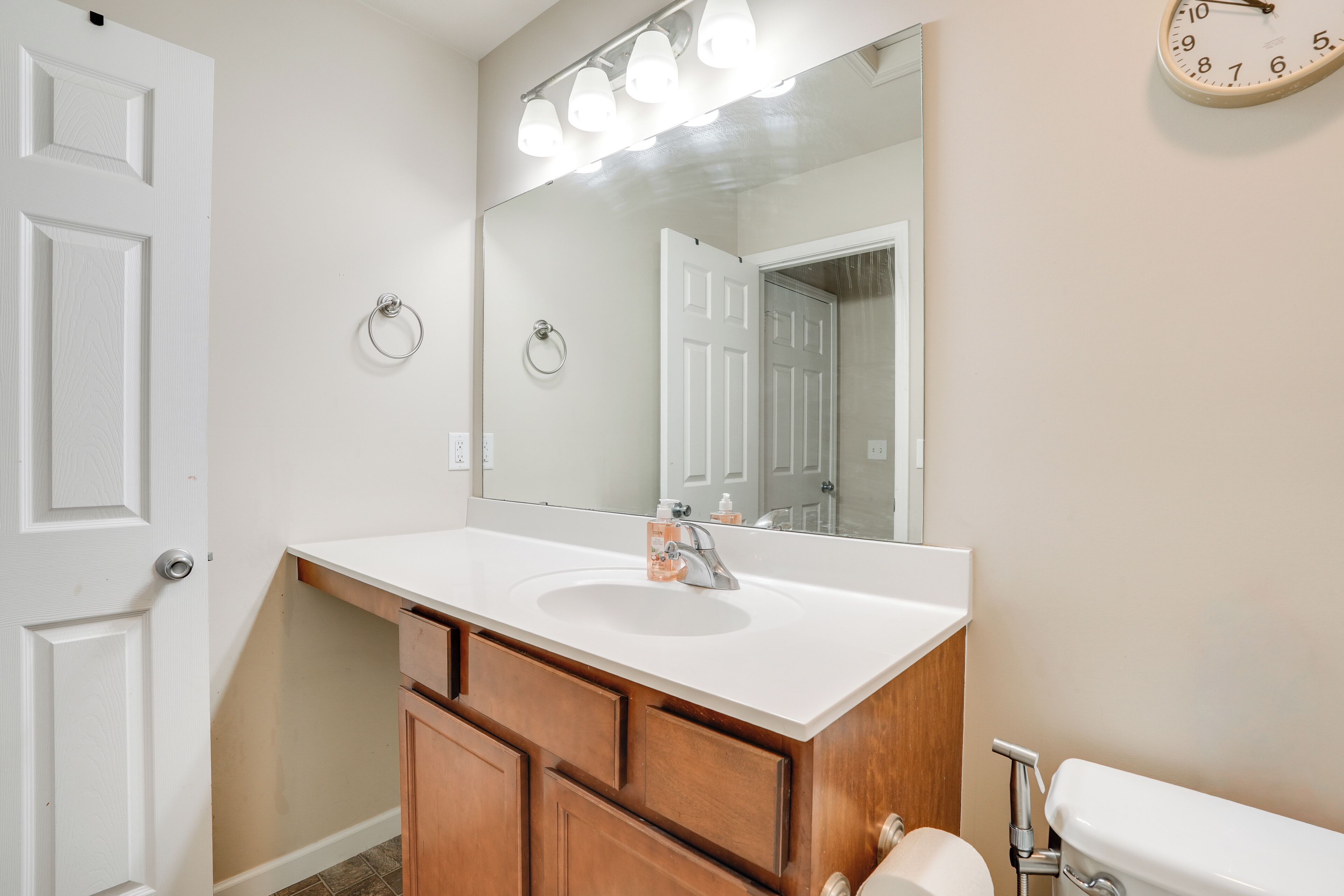 A bathroom with a white sink, wooden cabinets, a large mirror, and a toilet.