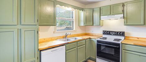 A kitchen with green cabinets, a white dishwasher, a stove, and a window with blinds.