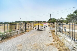 Uma entrada com portão e aviso, uma parede de pedra e um caminho de cascalho que leva a uma área cercada.