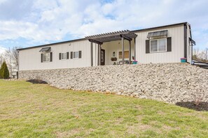 A single-story building with a covered patio area, a stone retaining wall, and a small garden. - Spacious Patio & Yard! Family Home in Byrdstown (Byrdstown)