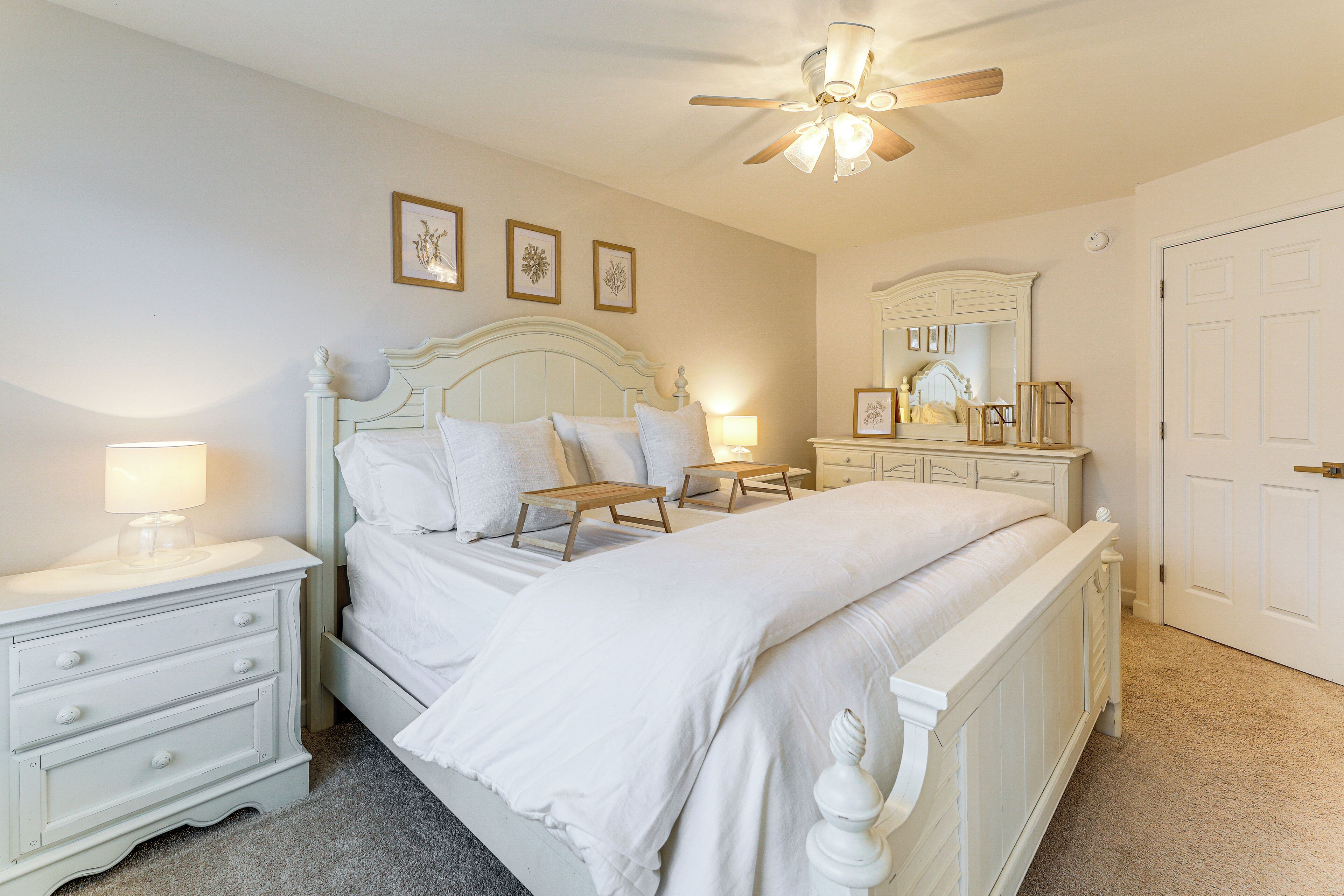 A bedroom with a white bed, nightstands, a ceiling fan, and a door.