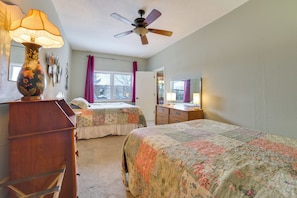 Une chambre avec deux lits, une commode, un ventilateur de plafond, une fenêtre avec des rideaux et un miroir.