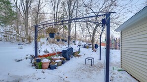Un giardino innevato con un gazebo in metallo, piante in vaso e un deposito.