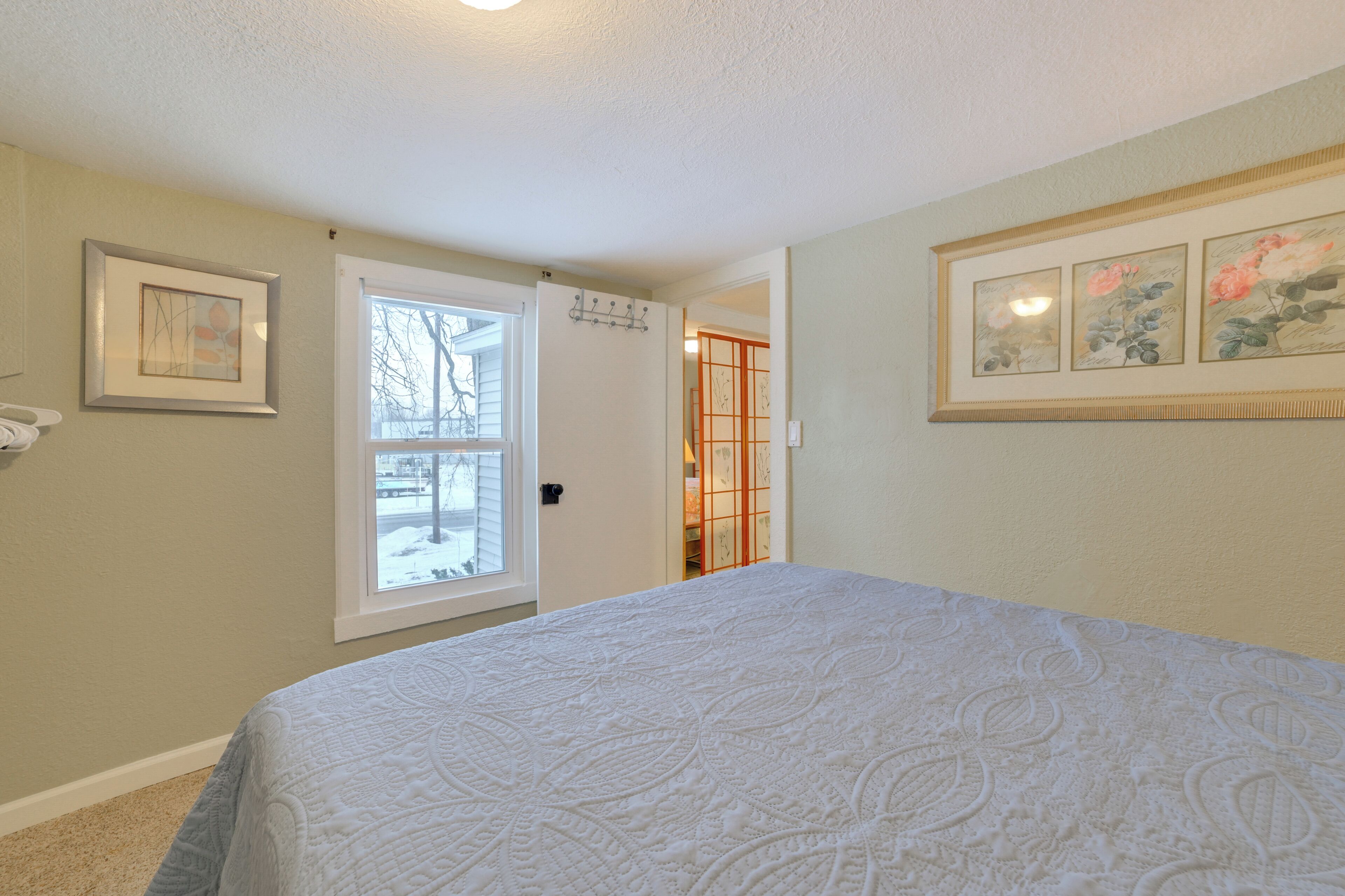 A bedroom with a large bed, a window, and a door leading to a hallway.
