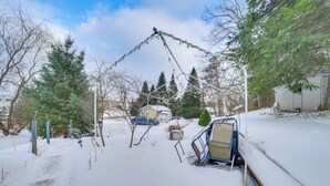 Una zona residenziale innevata con un vialetto coperto di neve, un'auto blu e una piccola casa sullo sfondo.