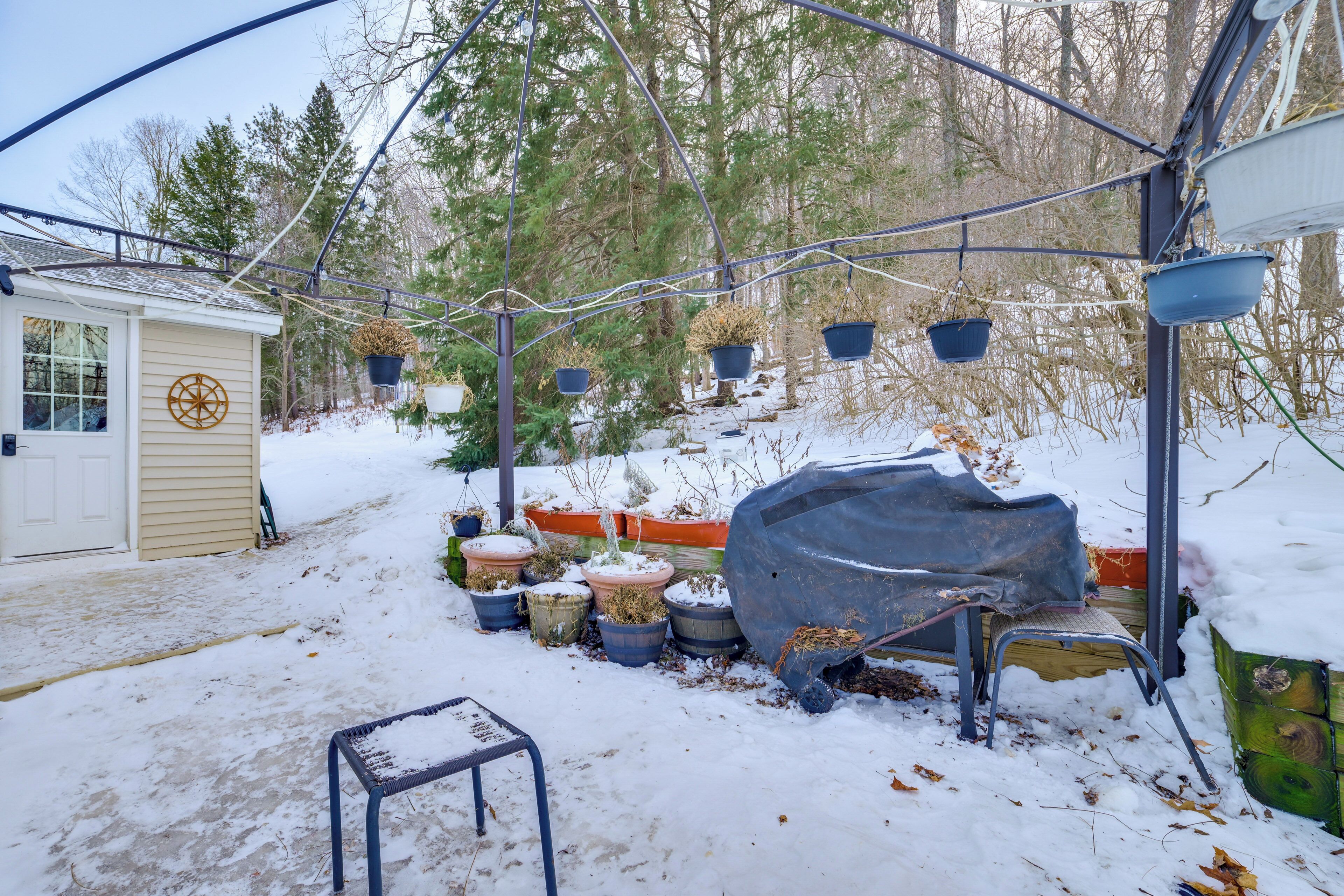 A snow-covered garden with potted plants and a covered bench.