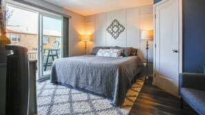 A bedroom with a large bed, two bedside lamps, a decorative wall piece, and a sliding glass door to a balcony. - Steps to Brigantine Beach: New Jersey Beach Condo (Brigantine)