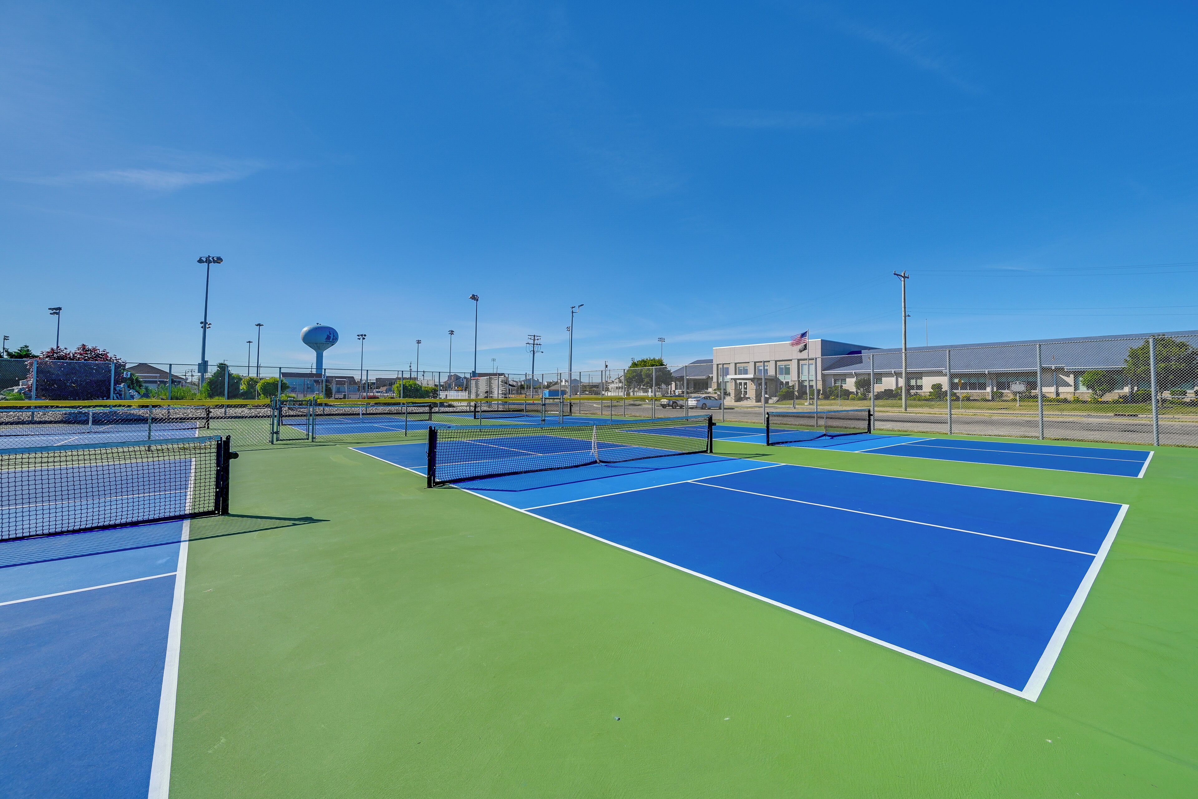 Tenniskenttä, jossa on useita pelikenttiä, verkko ja kentän ympärillä oleva aita.