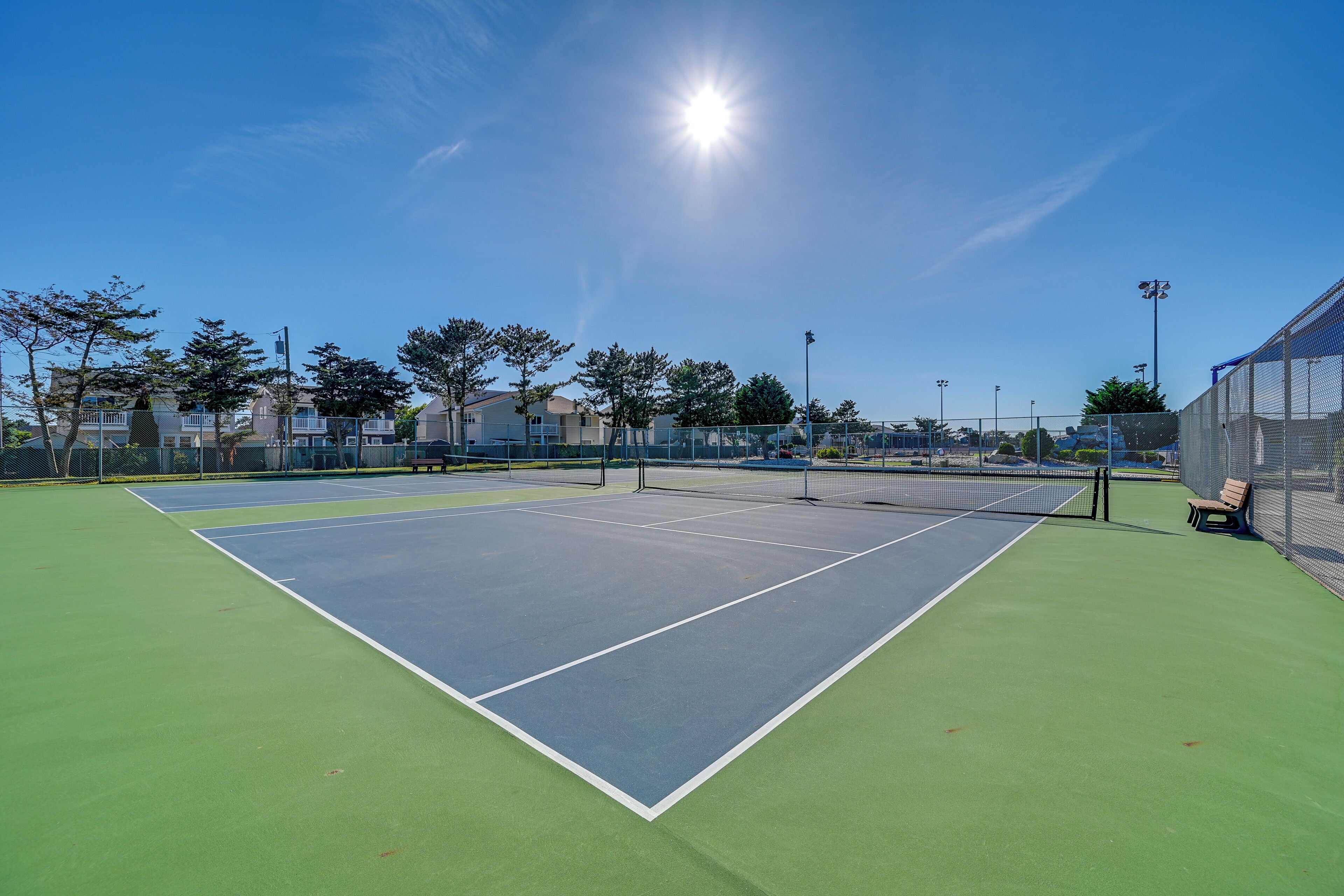 Ein Tennisplatz mit Netz, umzäumt von einem Zaun, und einer Bank.