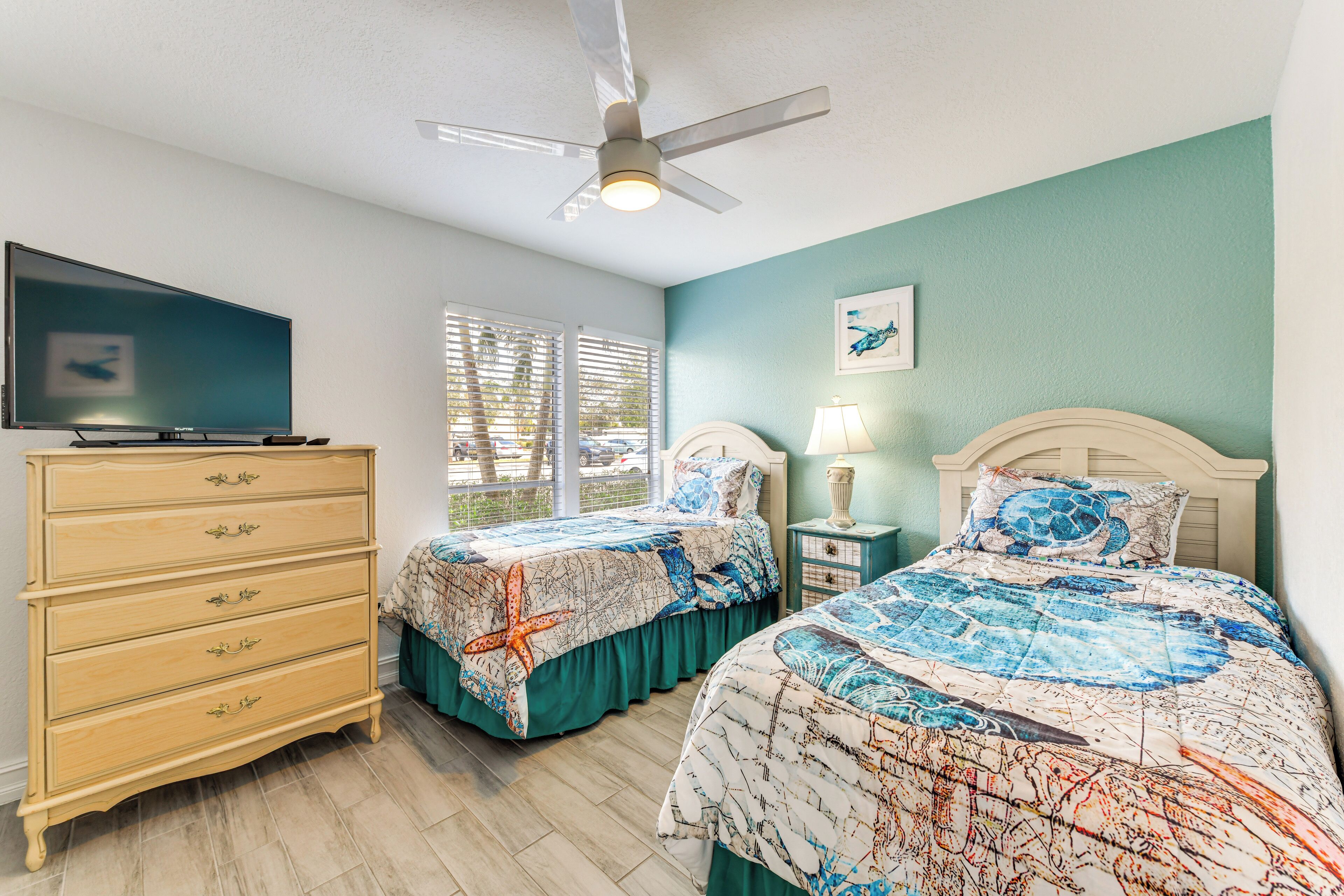 Une chambre avec deux lits, une commode, un ventilateur de plafond et un téléviseur.