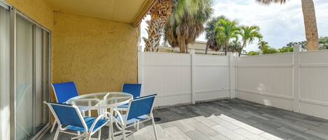 A covered patio with a table and chairs, a white fence, and palm trees in the background.