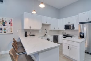 A modern kitchen with white cabinets, a stainless steel refrigerator, a microwave, and a large island with bar stools. - Steps to Casinos & Shuttle! Central City Home Base (Black Hawk)