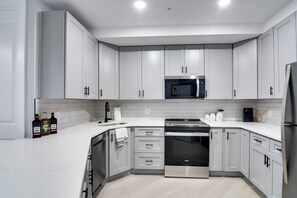 Una cocina moderna con armarios blancos, electrodomésticos de acero inoxidable y encimera blanca.