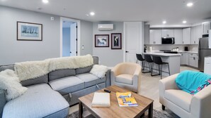 Ein modernes Wohnzimmer mit einem grauen Sofa, einem Holztisch und einer Küche im Hintergrund.