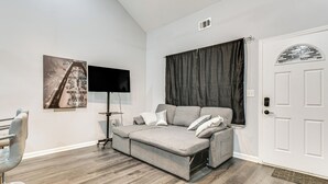 A modern room with a sofa bed, a flat-screen TV, a chair, and a door with a decorative glass panel. - Easy I-85 Access! Quiet Fairburn Extended Stay (Fairburn)