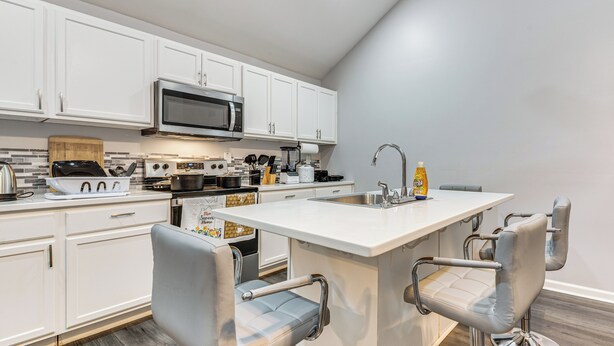 A modern kitchen with white cabinets, a stainless steel microwave, a built-in oven, and a central island with bar stools. - Easy I-85 Access! Quiet Fairburn Extended Stay (Fairburn)