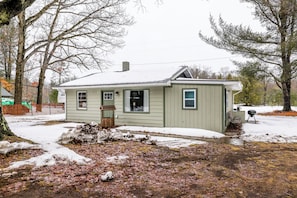 A single-story house with a front porch, a chimney, and a snow-covered yard. - Fish, Bike & Hike! Wooded Irons Getaway Near River (Irons)