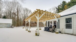 Un patio cubierto con un pérgola de madera, plantas en macetas y una zona de estar.