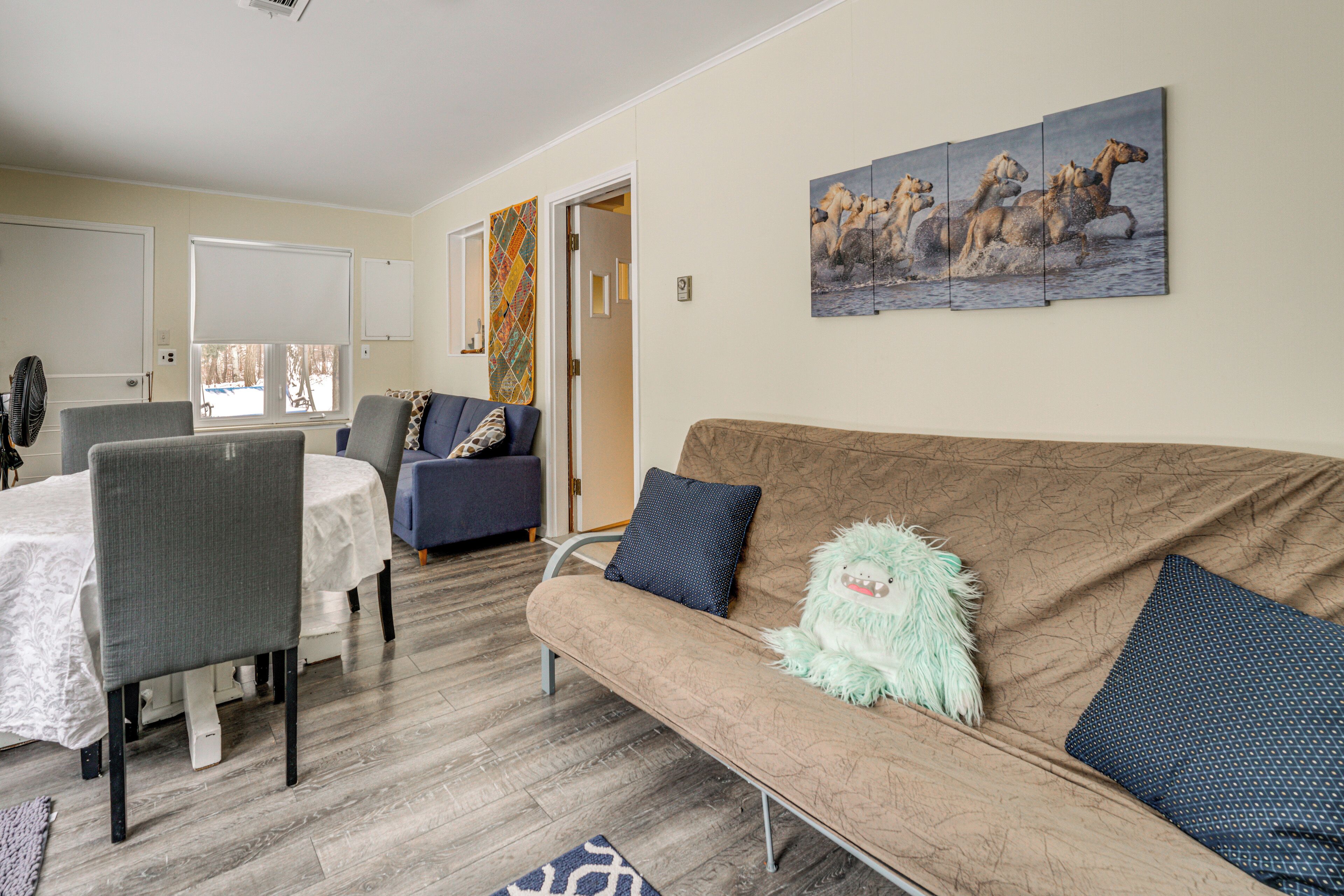 A living room with a brown sofa, a dining table with chairs, and a painting of horses on the wall.