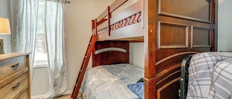 A bunk bed with a wooden headboard, a dresser with drawers, a patterned rug, and a window with curtains.