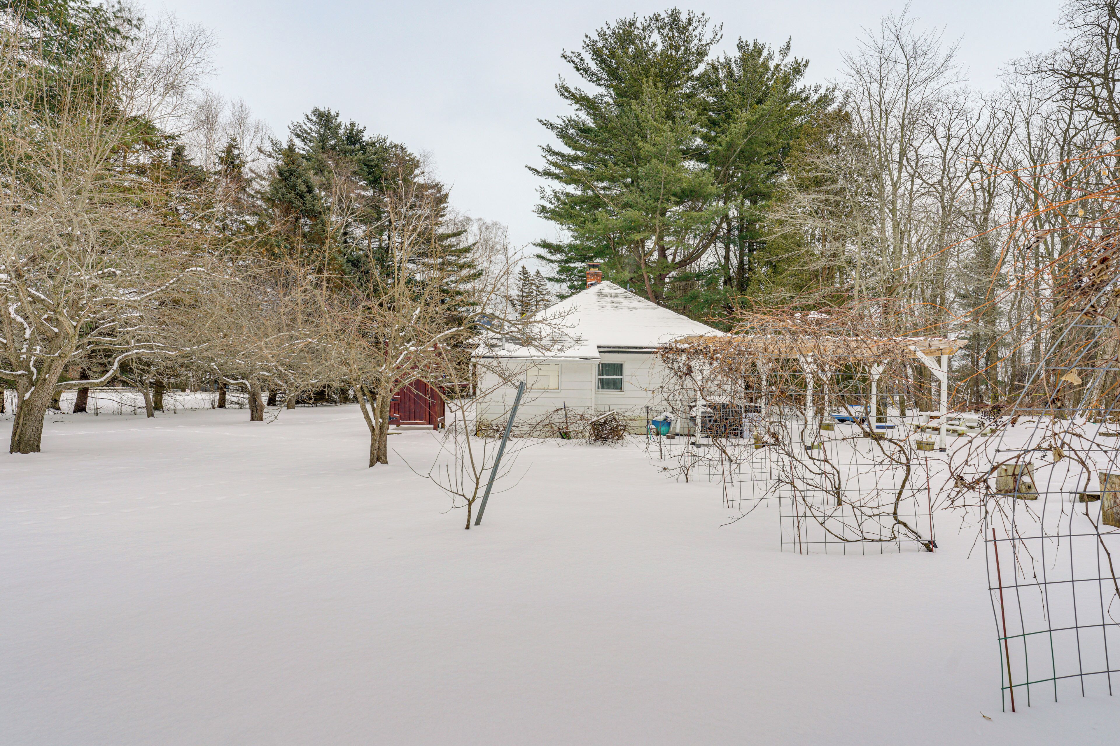 A snow-covered landscape with a house, trees, and a fenced area.