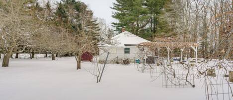 A snow-covered landscape with a house, trees, and a fenced area.