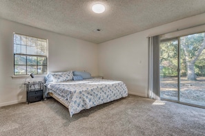 A bedroom with a bed, a nightstand, a window, and a sliding glass door leading to an outdoor area. - Beach Gear & Cruiser Bicycles: Quiet Pensacola Gem (Pensacola)
