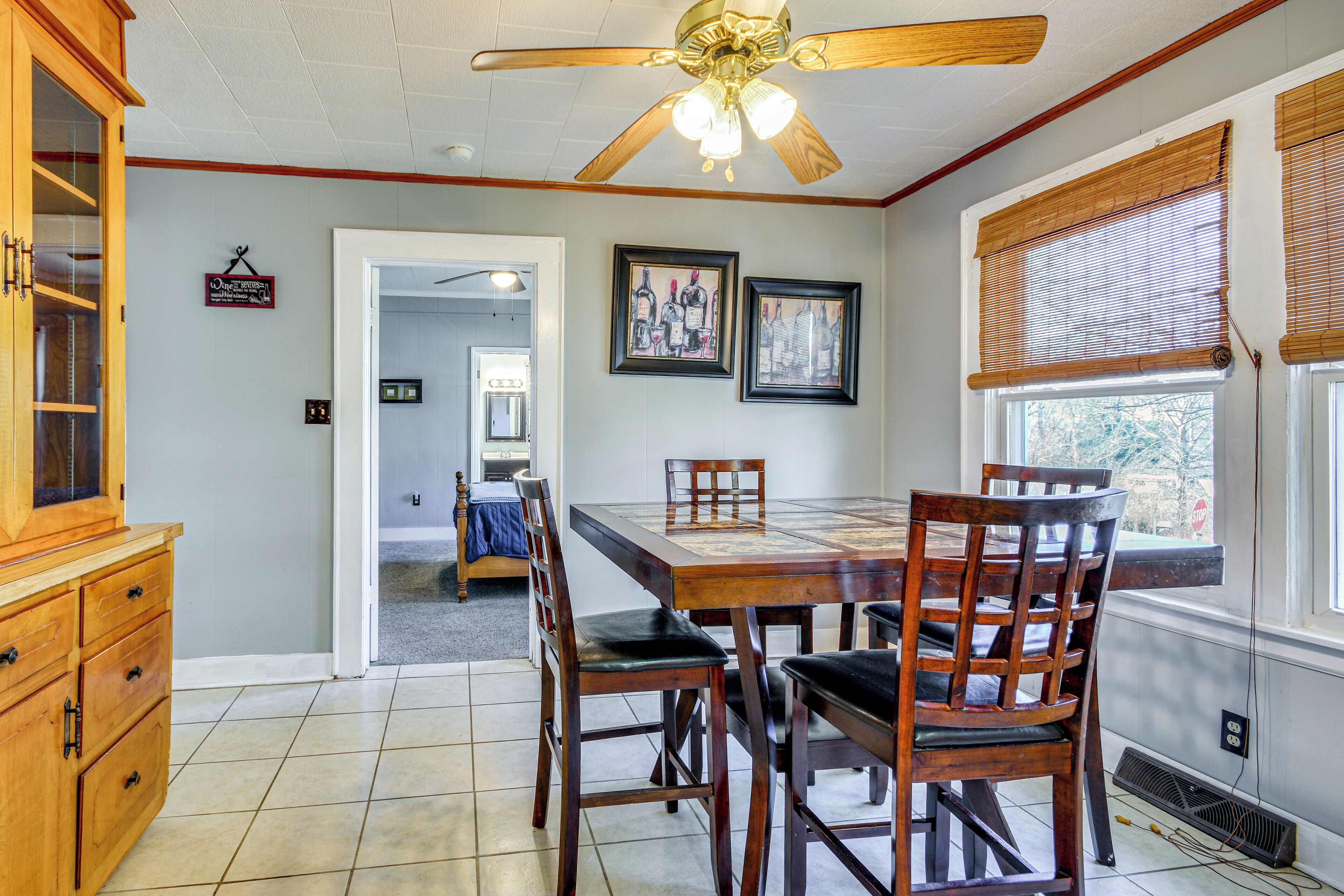 A dining area with a wooden table and chairs, a ceiling fan, and framed artwork on the wall.