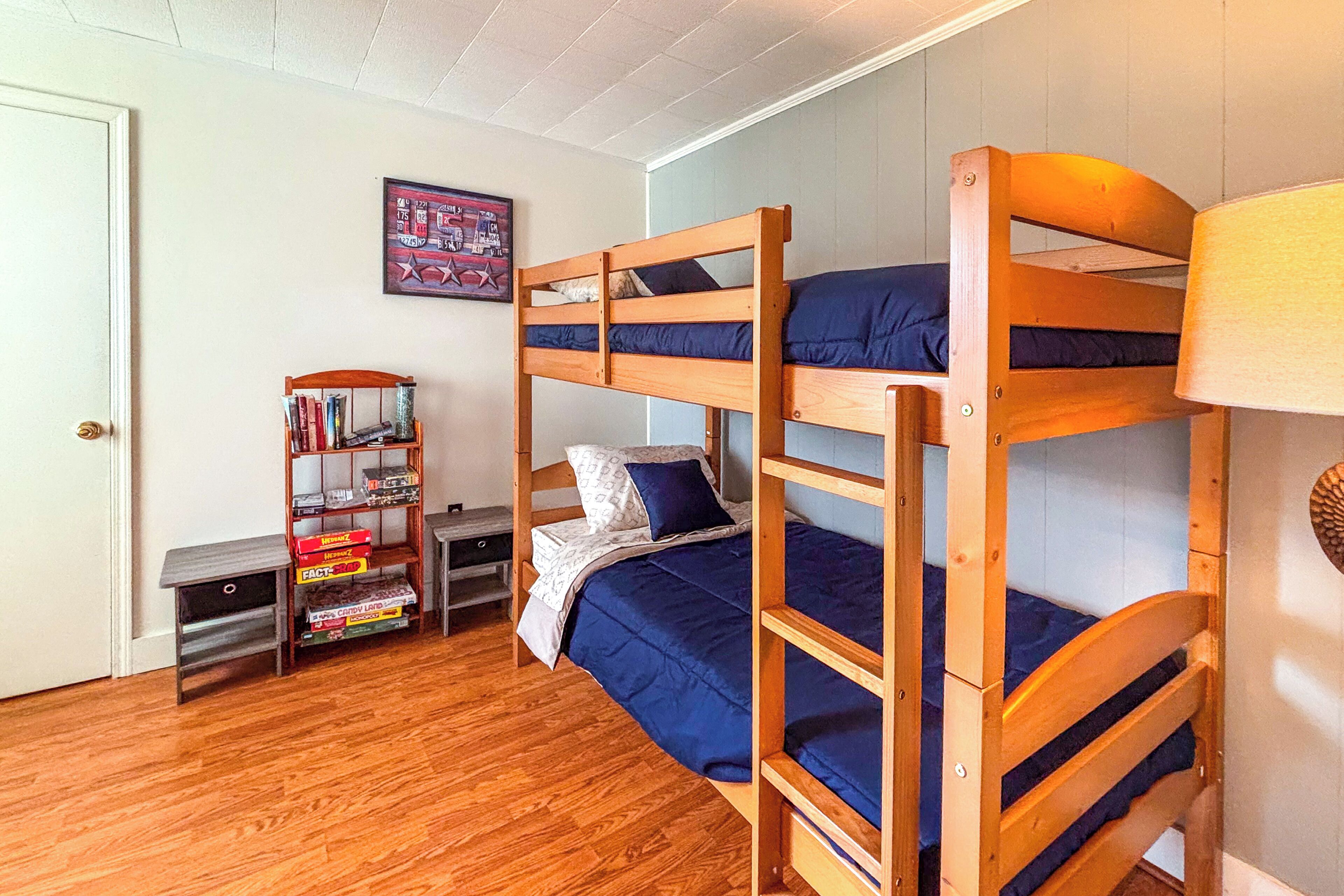 A bunk bed room with a wooden floor, a bookshelf, and a lamp.