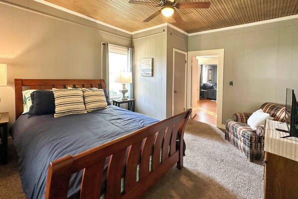 A bedroom with a wooden bed, a ceiling fan, a nightstand, a lamp, a plaid sofa, and a television. - 'the Vineyard House' - 2 Mi to Dtwn Mount Airy! (Mount Airy)