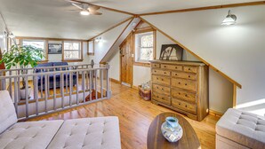 A spacious loft bedroom with a sloped ceiling, wooden beams, a large dresser, a sofa, and a dining table. - Bring Your Boat! Woodsy Cottage Near Fayetteville (Fayetteville)