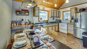 A kitchen with wooden cabinets, a stainless steel refrigerator, and a dining table set for four. - Bring Your Boat! Woodsy Cottage Near Fayetteville (Fayetteville)