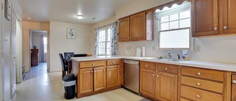 Una cocina con armarios de madera, lavavajillas y una ventana con cortinas.