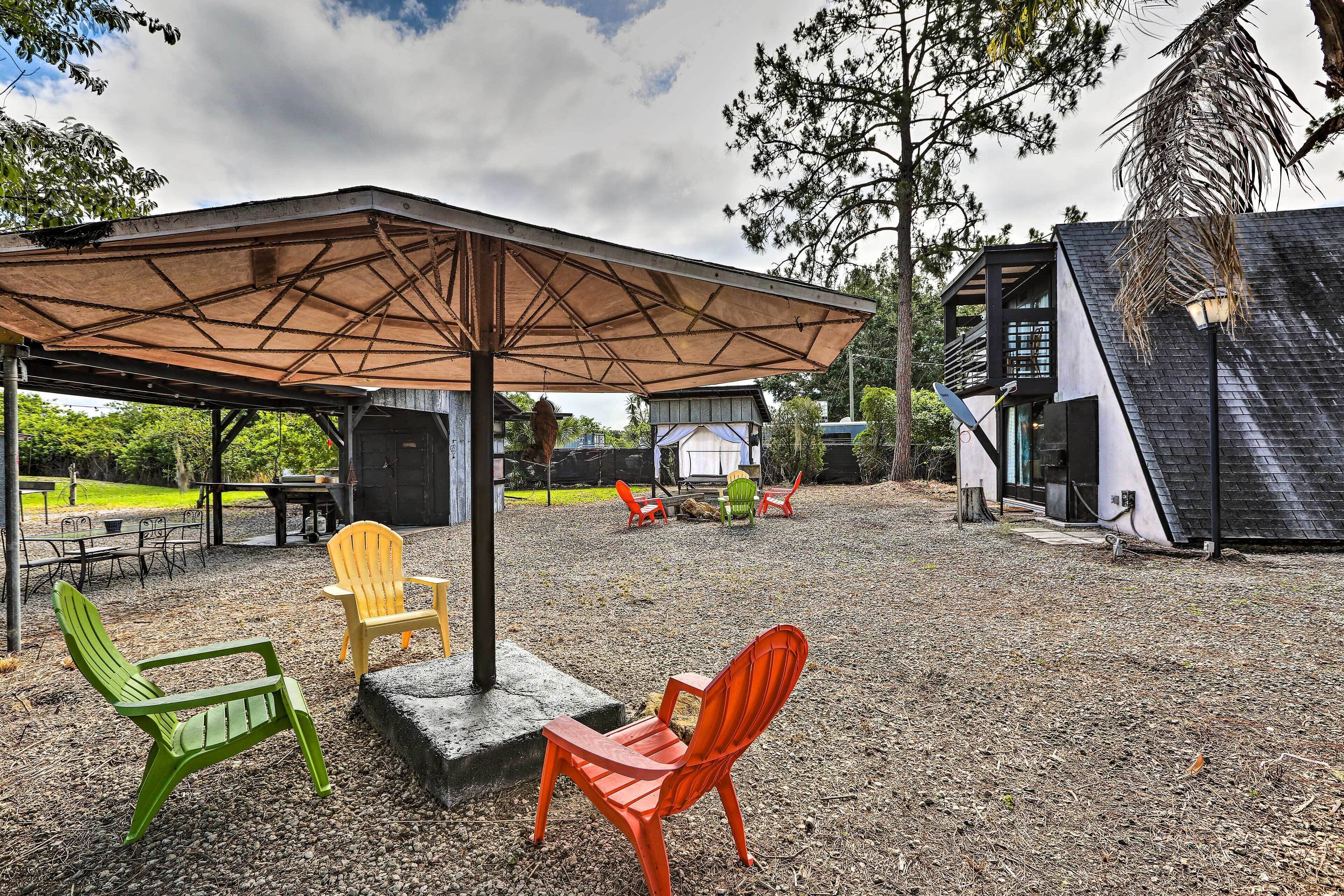 Un área de estar al aire libre con un patio cubierto, sillas exteriores y un edificio al fondo.