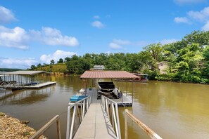 A dock with a covered boat house, a small boat, and a docked boat. - 3BR Lakefront Home w/ 2 Living Rooms, Dock & W/D (Climax Springs)