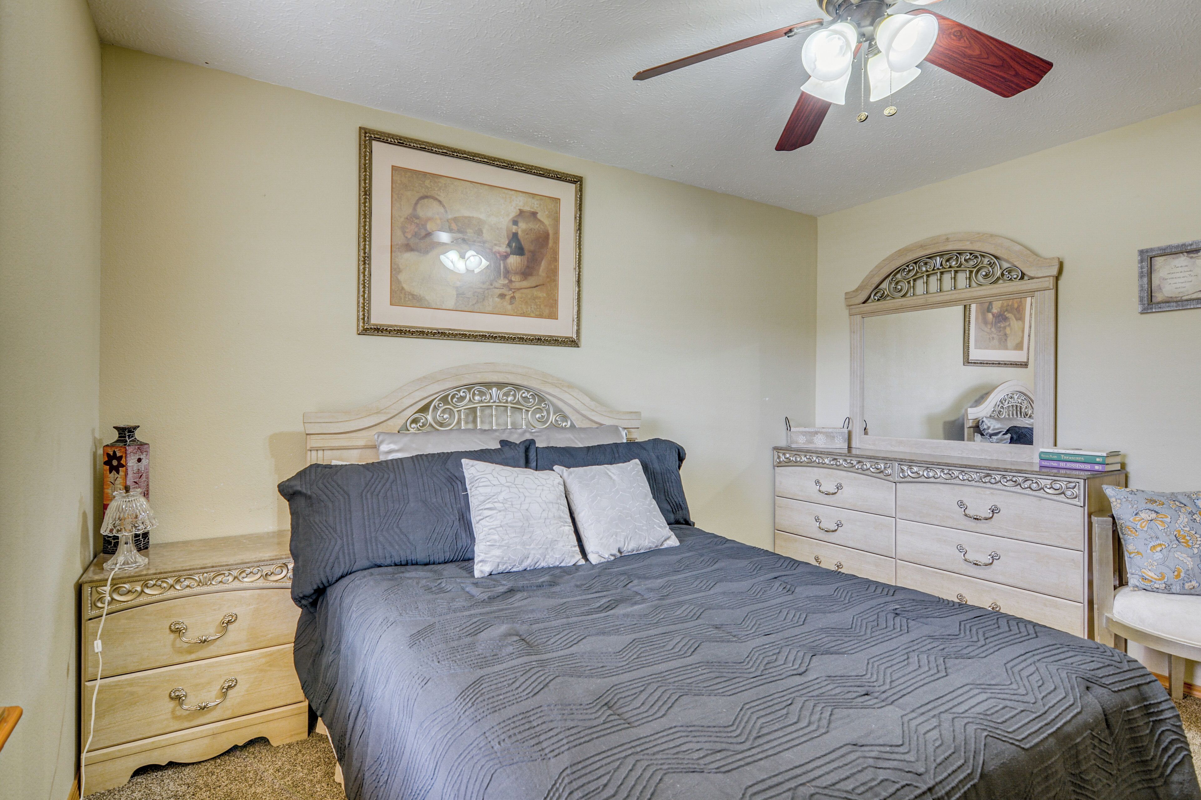 A bedroom with a bed, nightstands, a dresser, a ceiling fan, and wall art.