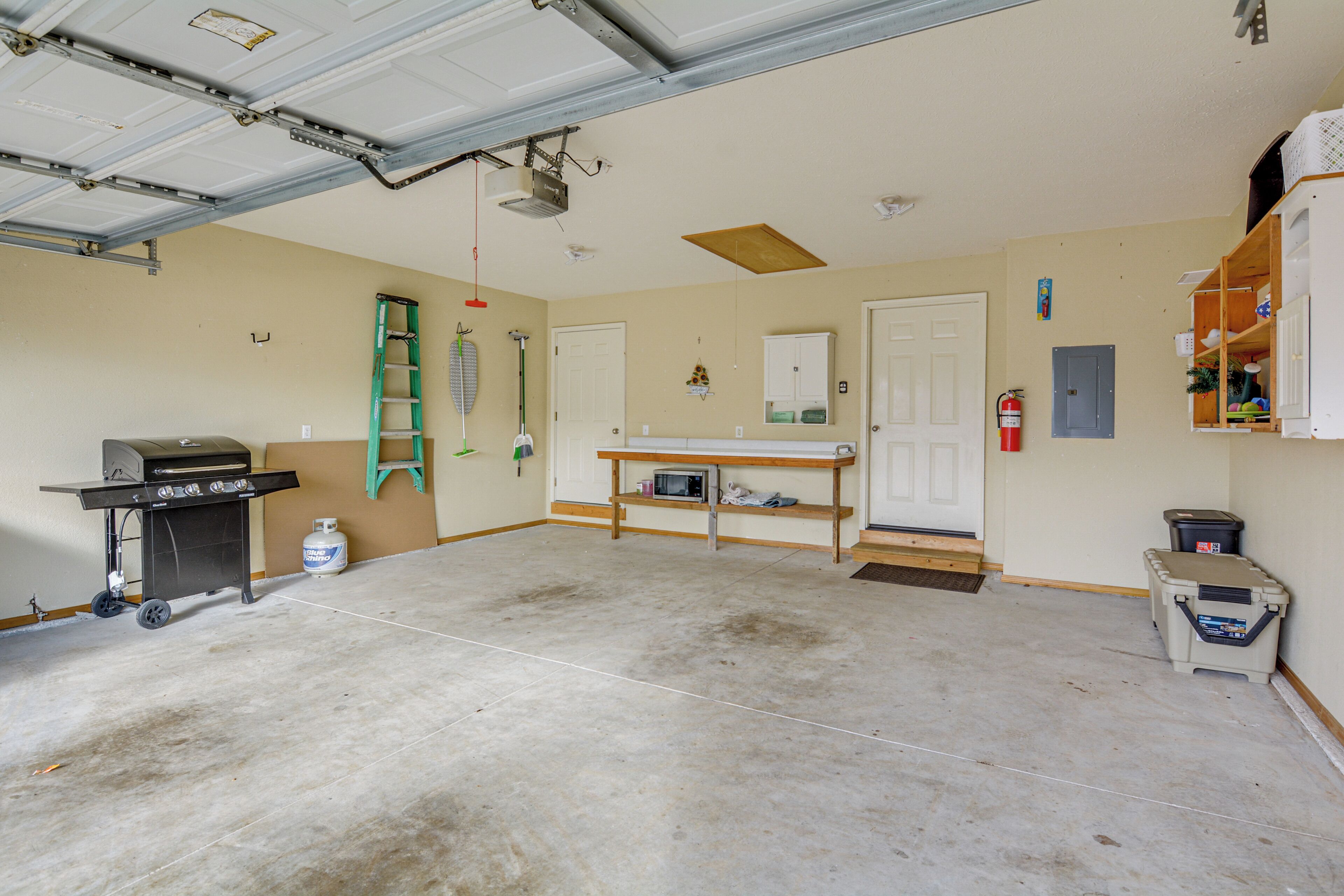 Eine Garage mit Betonboden, Grill, Leiter, Regalen und Feuerlöscher.