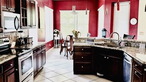 A kitchen with dark wooden cabinets, a granite countertop, a built-in oven, and a large island with a sink. - SamAria - Two-story Villa (Deltona)