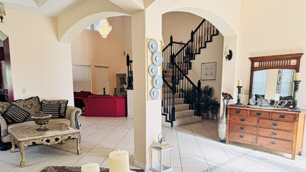 A spacious living room with a sofa, a coffee table, and a fireplace. There is a staircase leading to another level, and a wooden cabinet with drawers. - SamAria - Two-story Villa (Deltona)