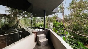 Un balcon extérieur moderne, doté d’une paroi vitrée, d’un petit escalier et entouré d’une végétation luxuriante.