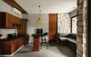 A modern kitchen with wooden cabinets, a central island, and a stone accent wall. - Siwa Jungle Romance C1-002 Beach Club Access (Tulum)