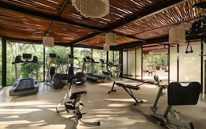 A gym with various exercise equipment, large windows, and a wooden ceiling. - Siwa Jungle Romance Lovely C1-002 Beach Club (Tulum)